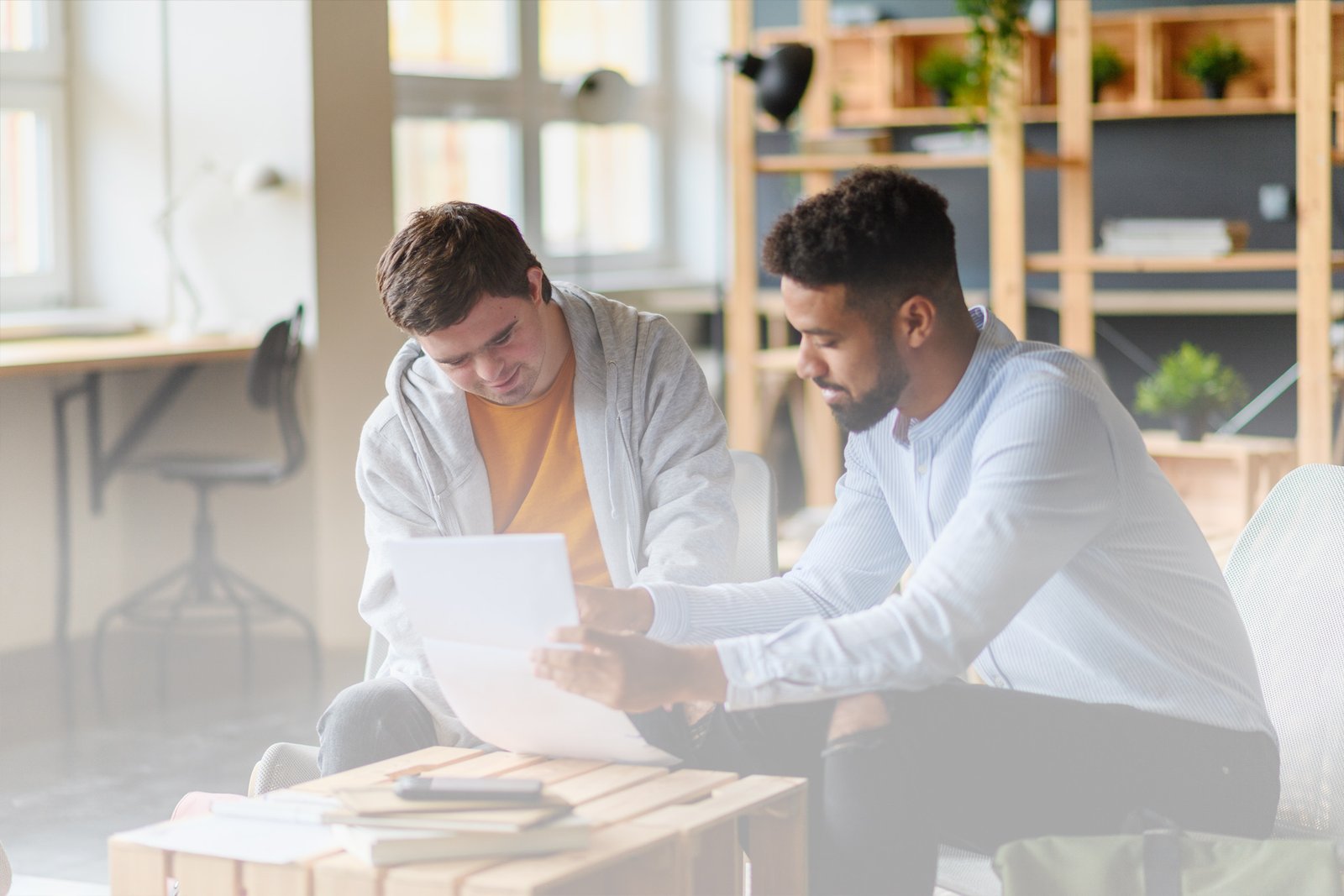 A male teacher guides a young adult male student with Down Syndrome through a worksheet.